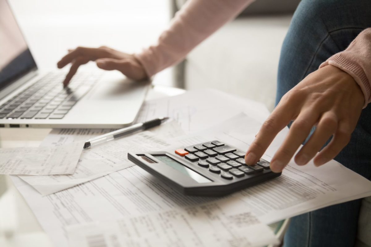 Conseil investissement immobilier Nantes – Mains de femme en gros plan calculant un budget avec une calculatrice un ordinateur et des factures