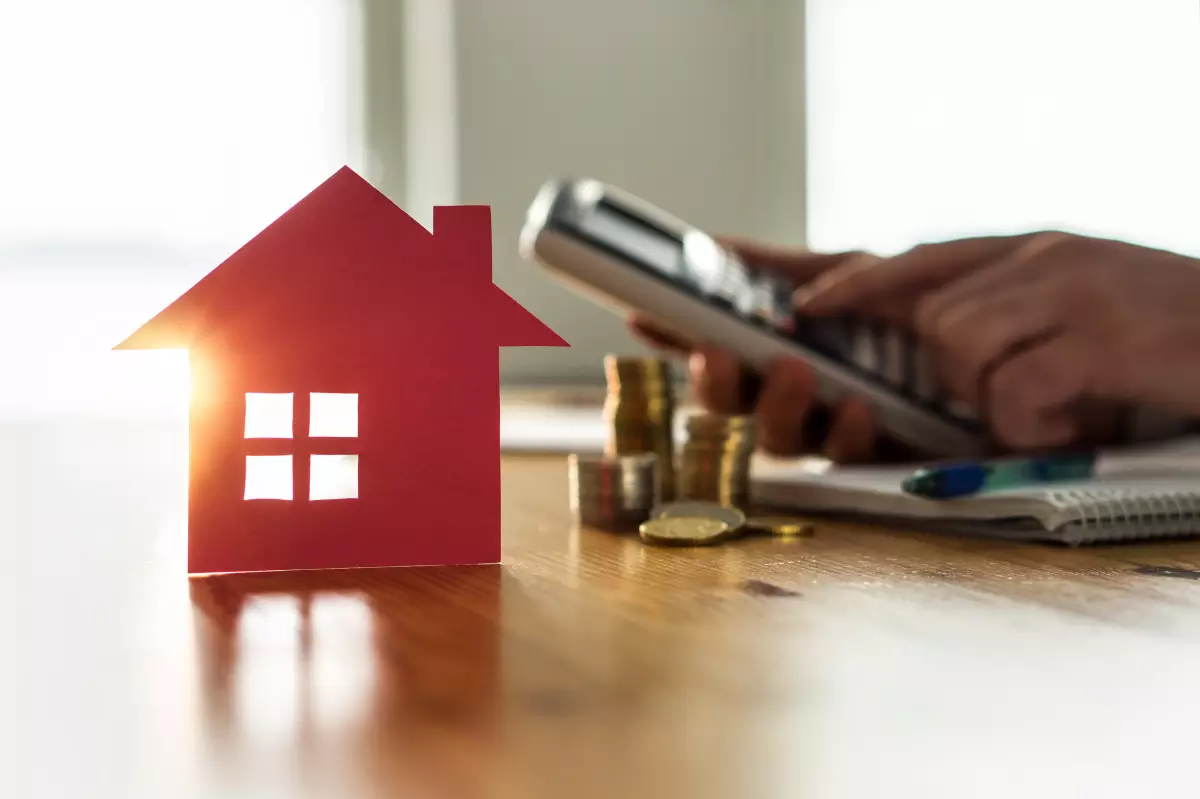 taxe logements vacants – une maison rouge avec une calculatrice et des pièces en fond