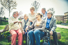 Maison partagée senior – Un groupe de personnes âgées discutant et riant sur un banc dans un parc