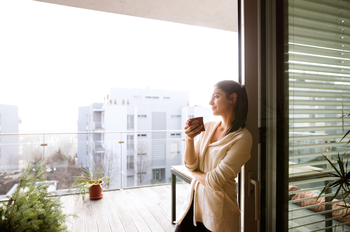 Prix appartement Nantes – Une femme boit son café sur la terrasse avec vue sur la ville de son appartement neuf