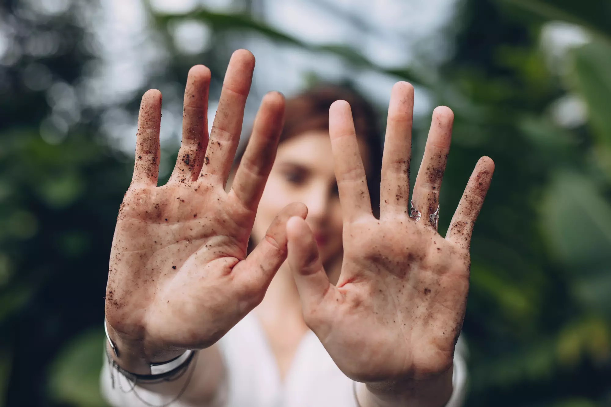 Une femme tend ses mains pleines de terre après avoir jardiner