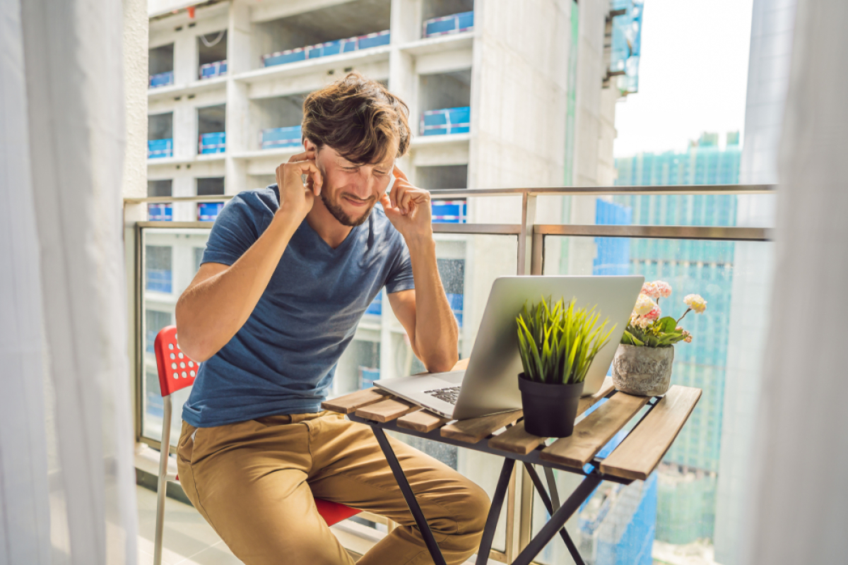 norme acoustique logement neuf – Un homme sur son balcon en train de se boucher les oreilles