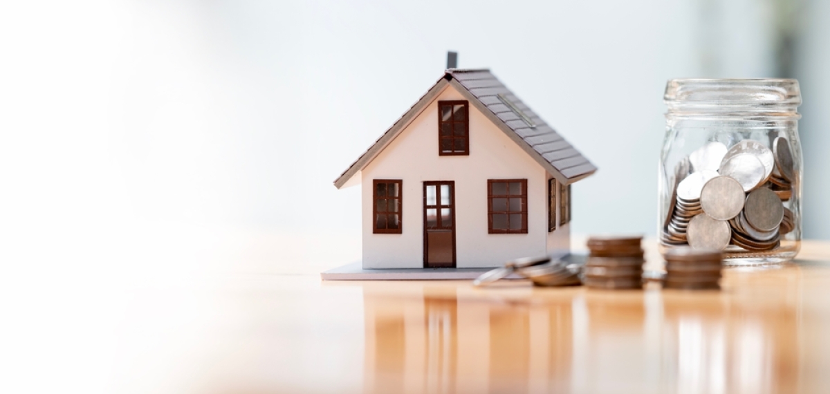 exonération taxe foncière logement neuf – Une maquette de maison posée à côté d'un bocal rempli de pièces de monnaie