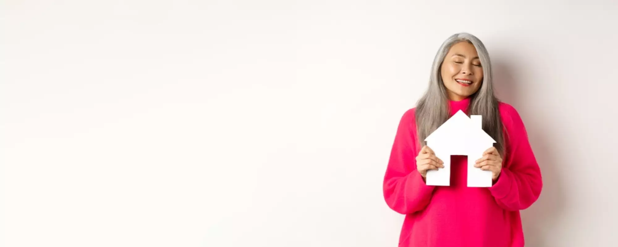 une femme en pull rose tient une petite maison en souriant