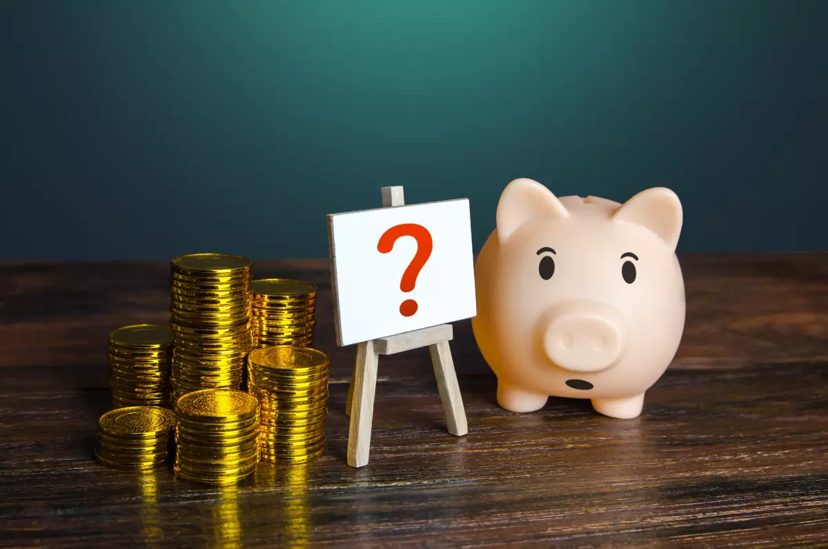 En 2024, il n’est quasiment plus possible d’emprunter sans apport pour un achat immobilier. une tirelire cochon, un tas de pièce et un chevalet portant un tableau blanc avec un point d’interrogation