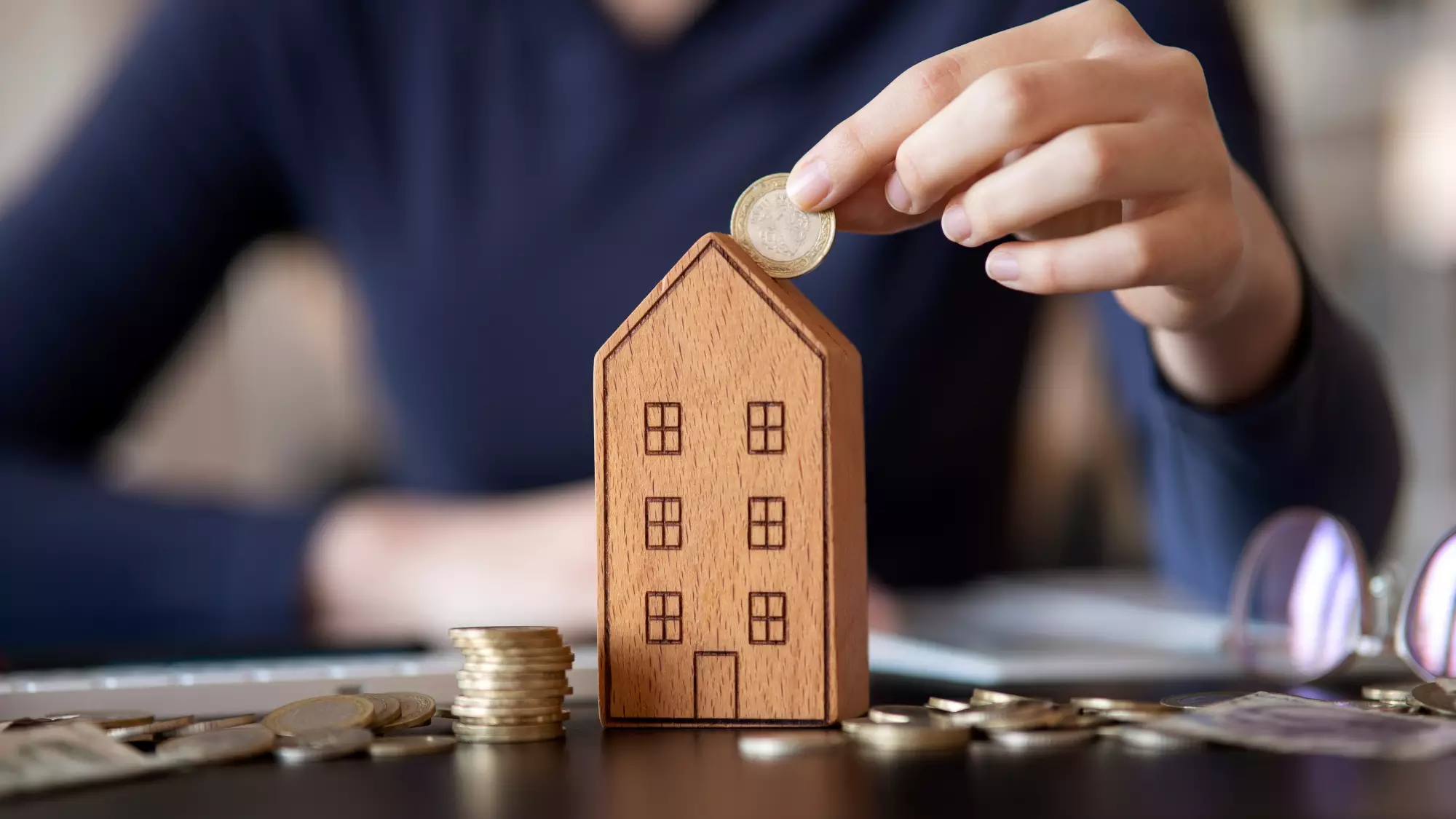 une main glisse un euro dans un bâtiment tirelire en bois