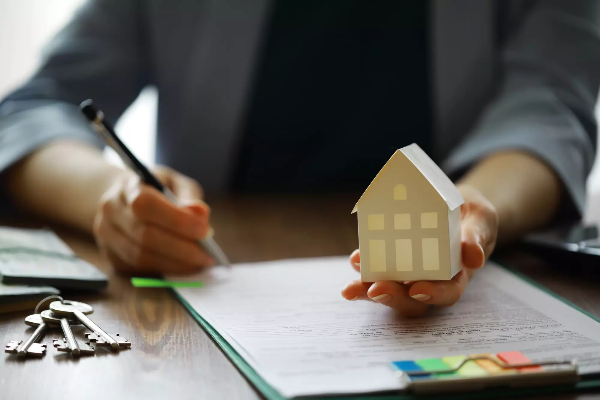 un homme signe un dossier d'une main et tient une maquette de maison de l'autre