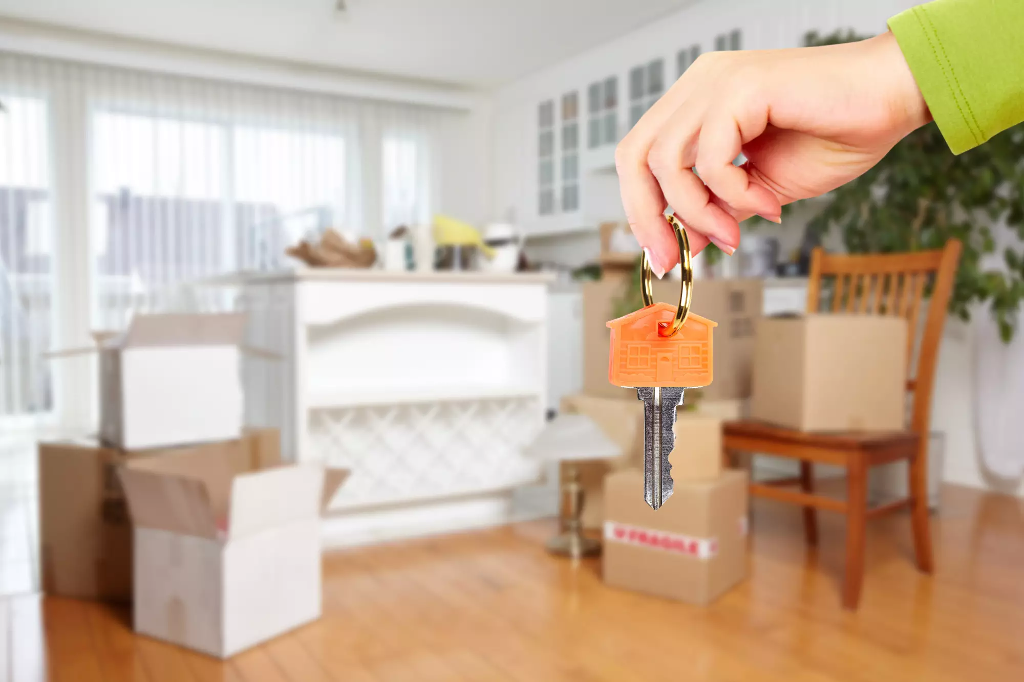 une clé tenu par une main féminine devant un logement meublé
