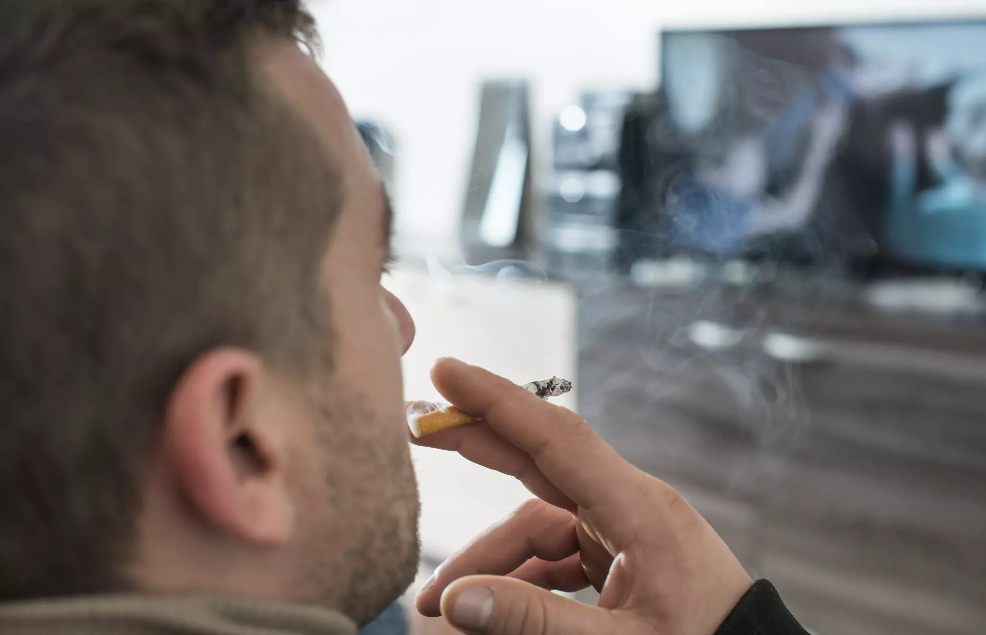 Un homme fume dans son appartement en regardant la télévision
